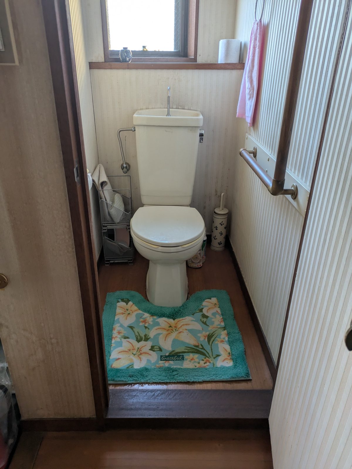改修前のトイレ。手洗い付きロータンクの洋式便器と木質の床