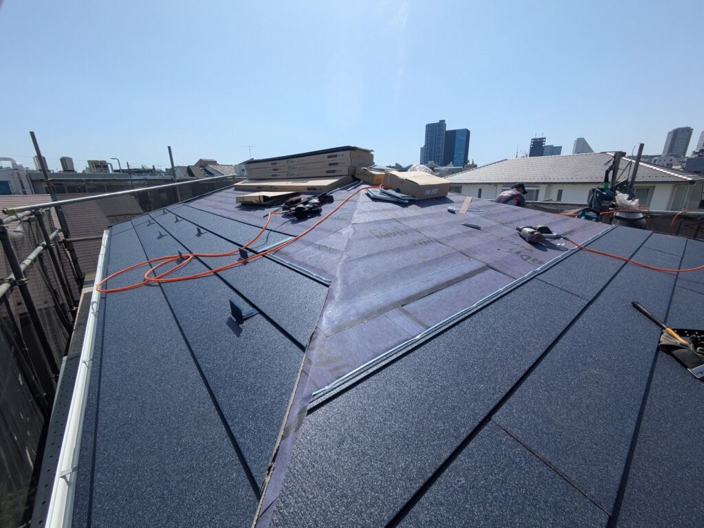 屋根カバー工法の施工中。手前は葺き上がったネイビーの金属屋根材、奥はまだルーフィングが見えている状態