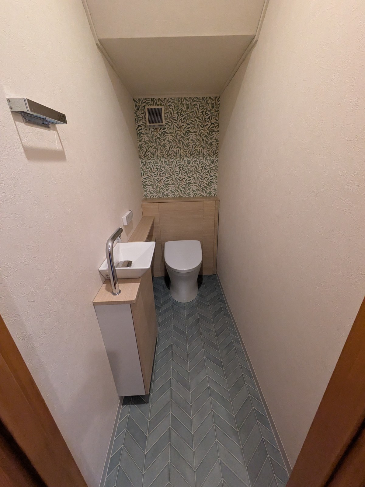 トイレの床。ブルーグレーのヘリンボーン柄と植物柄の壁