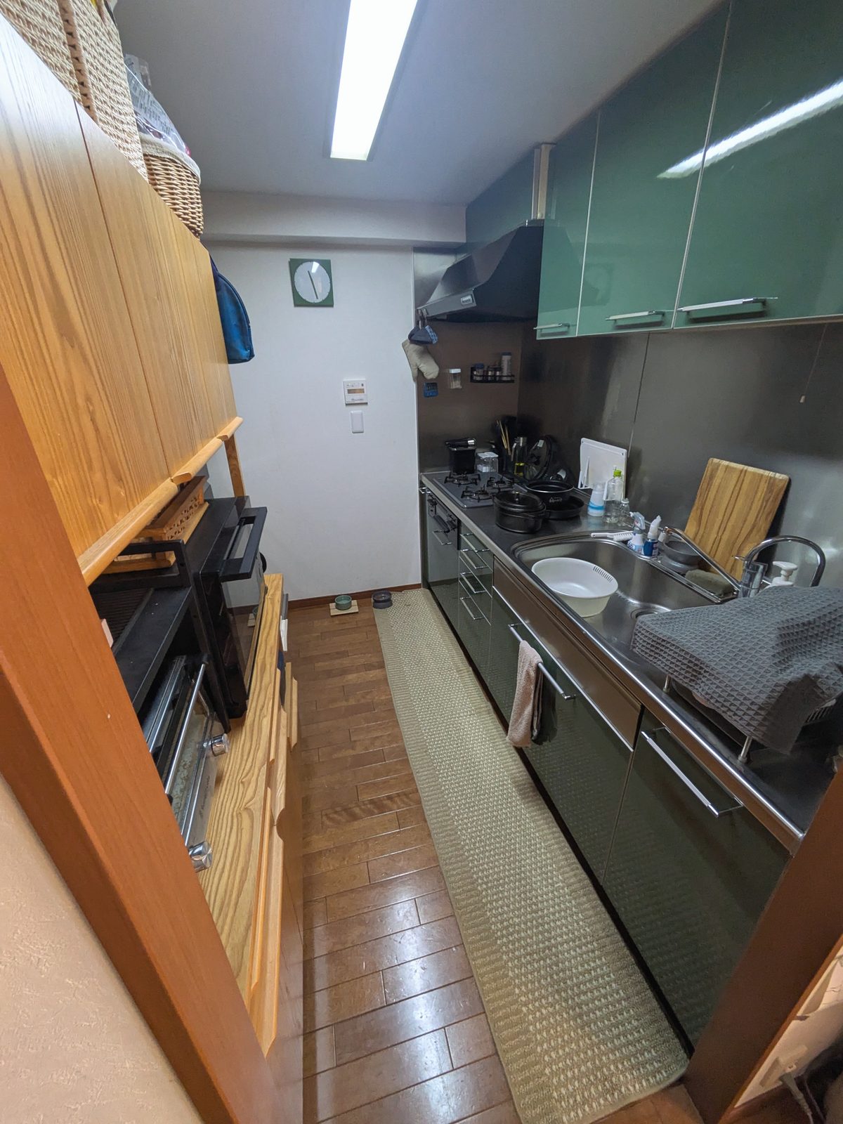 改修前のキッチン。木製カウンターと緑の吊戸棚、濃い色の既存の床