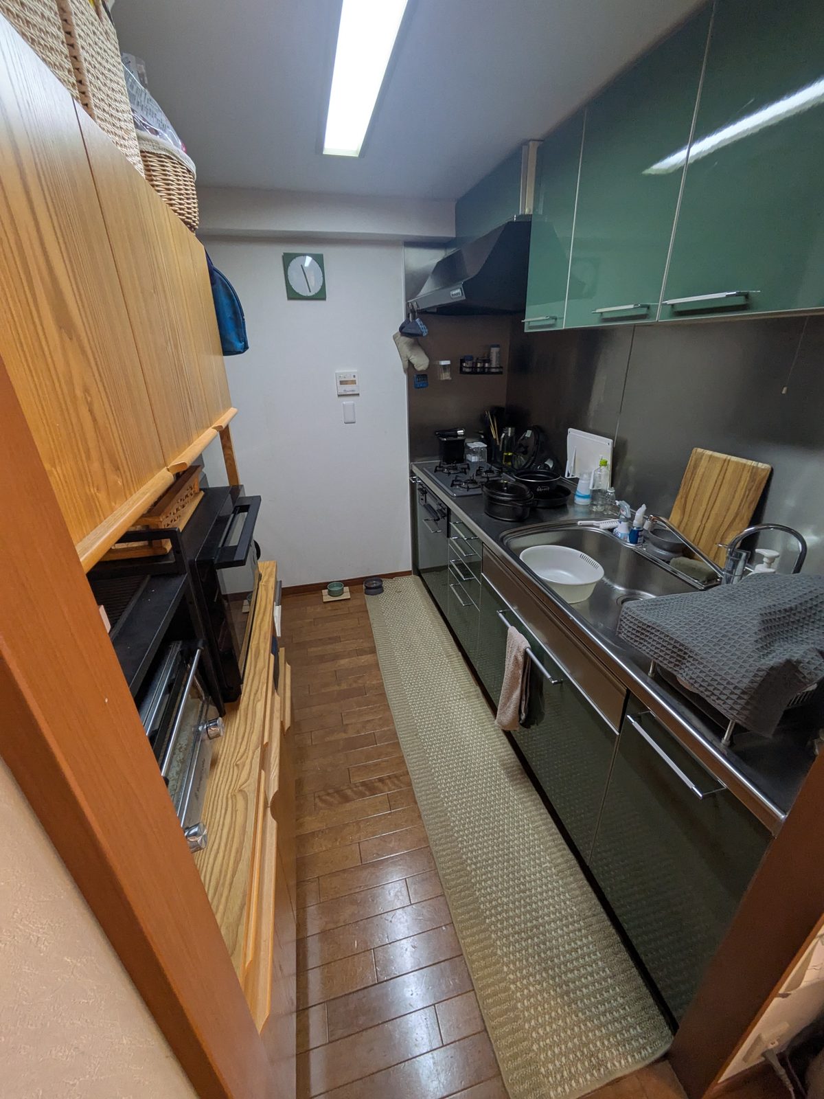 改修前のキッチン。木製カウンターと緑の吊戸棚、濃い色の既存の床